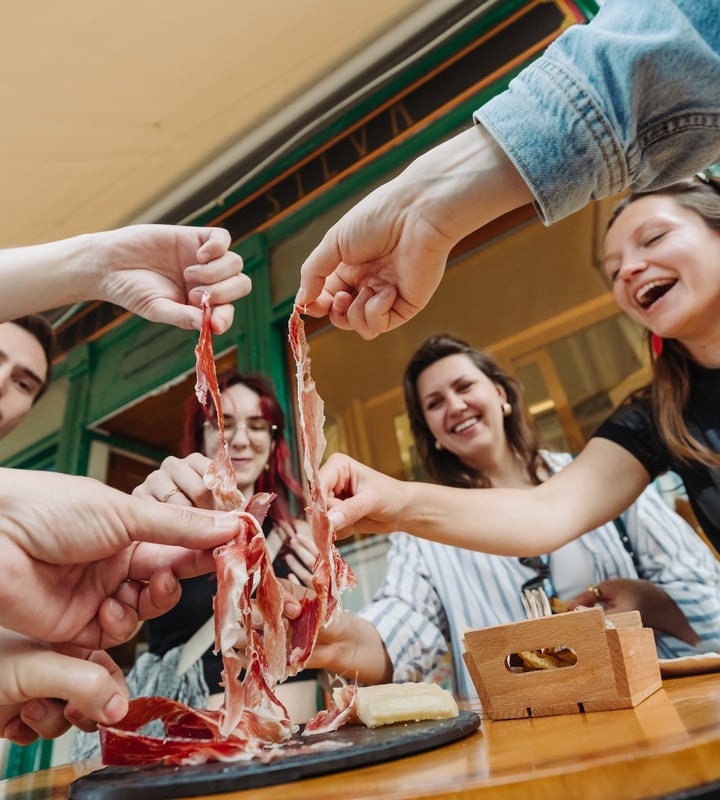 A group huddles around a plate of ham while exploring Lisbon on a food tour.